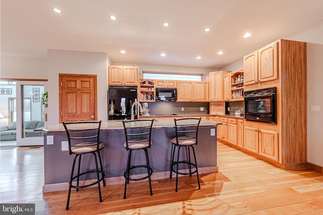 kitchen with a center island with sink, light wood-style floors, light brown cabinets, black appliances, and a kitchen breakfast bar