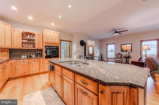 kitchen with light brown cabinets, oven, a sink, stainless steel dishwasher, and a center island with sink