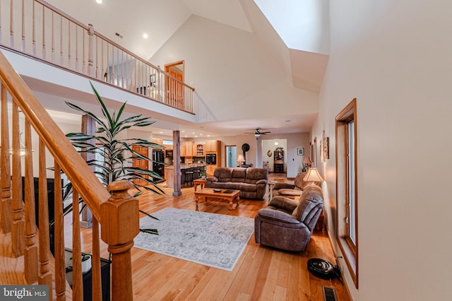 living area with hardwood / wood-style flooring, a high ceiling, visible vents, a ceiling fan, and stairway