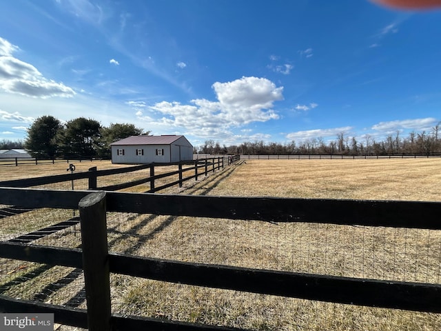 view of yard featuring an outbuilding, an enclosed area, a rural view, and an outdoor structure