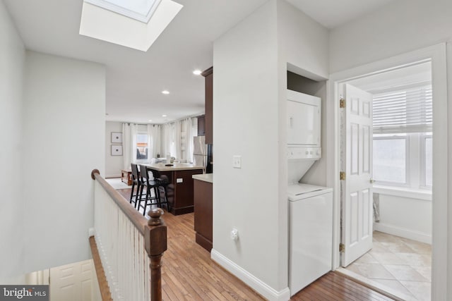 hallway featuring a skylight, baseboards, light wood-style floors, an upstairs landing, and stacked washing maching and dryer