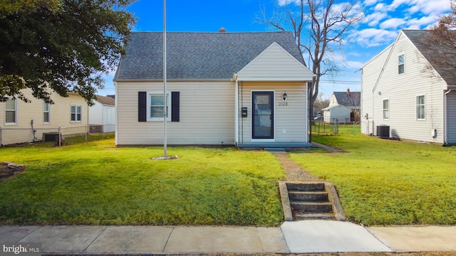 view of front of property with roof with shingles, fence, a front lawn, and central AC unit