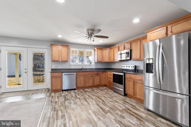 kitchen with appliances with stainless steel finishes, dark countertops, a sink, and light wood-style floors