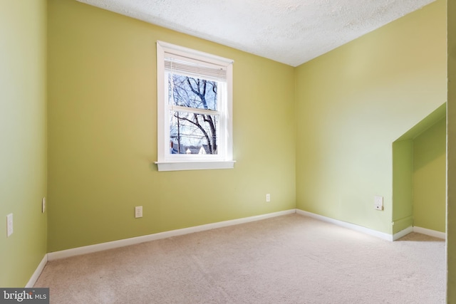 empty room with a textured ceiling, baseboards, and light colored carpet