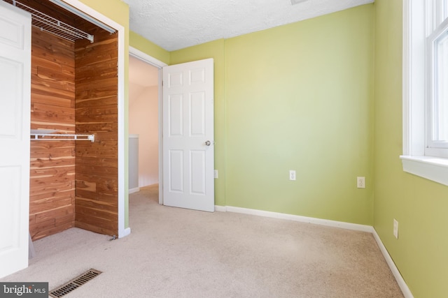 unfurnished bedroom with a textured ceiling, light colored carpet, wood walls, visible vents, and baseboards