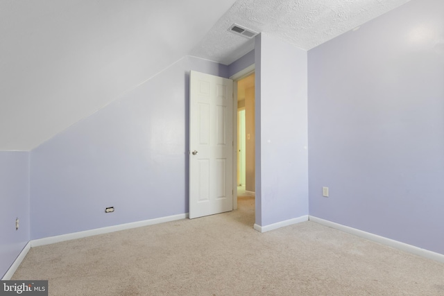 additional living space with baseboards, visible vents, light colored carpet, vaulted ceiling, and a textured ceiling