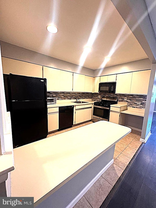 kitchen with light countertops, backsplash, white cabinets, a sink, and black appliances