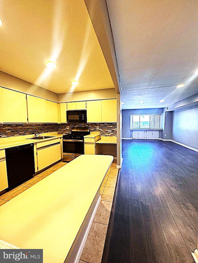 kitchen featuring light countertops, backsplash, a sink, wood finished floors, and black appliances