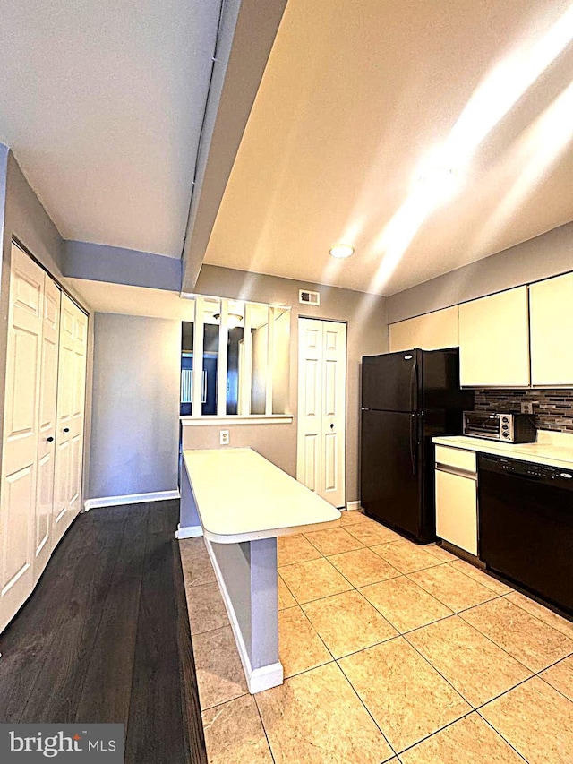 kitchen featuring a peninsula, visible vents, light countertops, black appliances, and tasteful backsplash