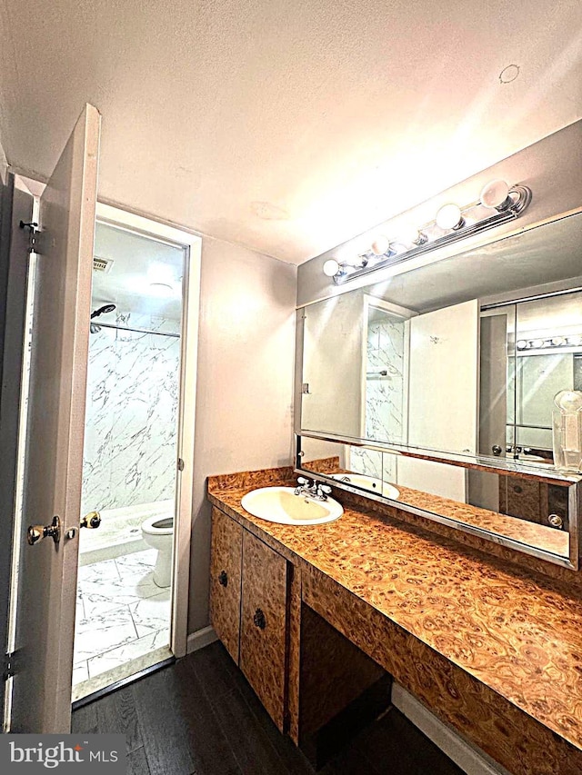 bathroom featuring a marble finish shower, toilet, wood finished floors, a textured ceiling, and vanity