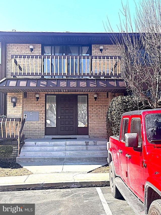 view of front facade featuring uncovered parking, covered porch, brick siding, and a balcony