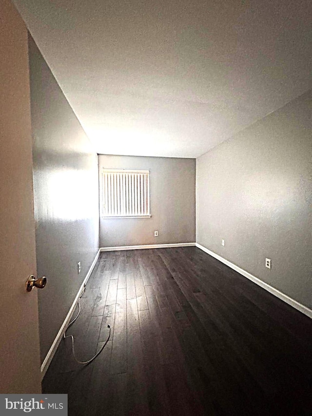 spare room featuring dark wood-style floors and baseboards