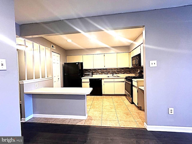 kitchen featuring decorative backsplash, white cabinets, light countertops, black appliances, and a sink