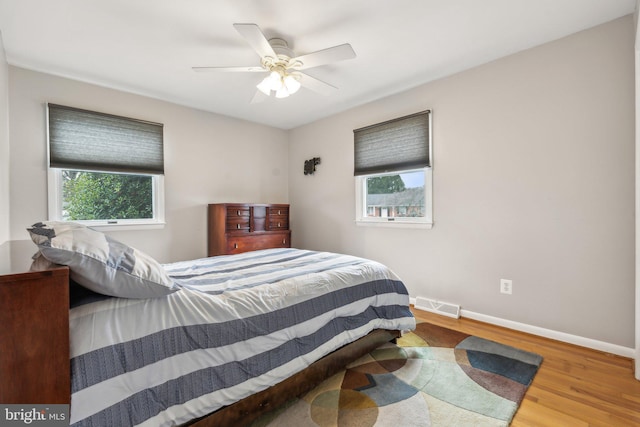 bedroom with a ceiling fan, visible vents, baseboards, and wood finished floors