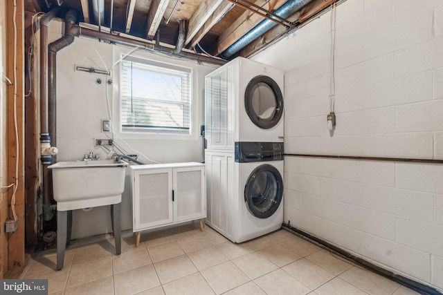 clothes washing area with concrete block wall, light tile patterned floors, laundry area, stacked washing maching and dryer, and a sink