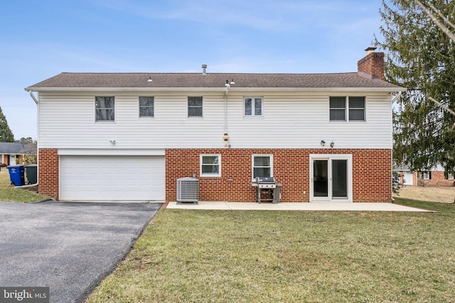 back of house featuring brick siding, a yard, a chimney, central air condition unit, and driveway