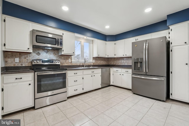 kitchen with stainless steel appliances, dark countertops, decorative backsplash, white cabinetry, and a sink