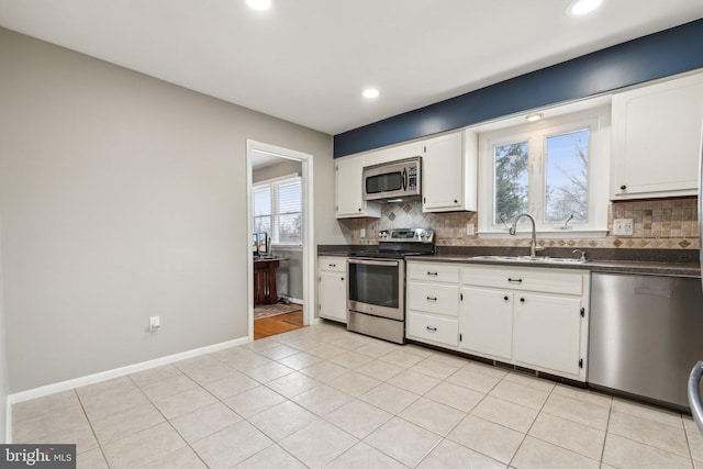 kitchen featuring stainless steel appliances, a sink, white cabinets, tasteful backsplash, and dark countertops