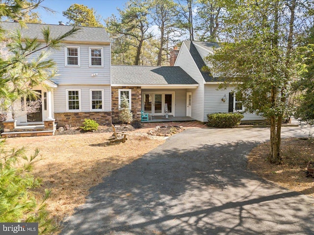 view of front of home with stone siding, a chimney, aphalt driveway, and roof with shingles