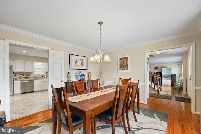 dining room with light wood-style floors, crown molding, an inviting chandelier, and stairs