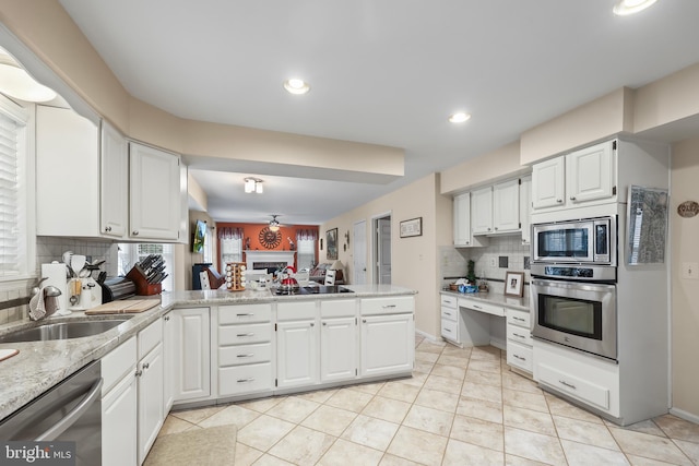 kitchen featuring white cabinets, appliances with stainless steel finishes, a peninsula, a fireplace, and a sink