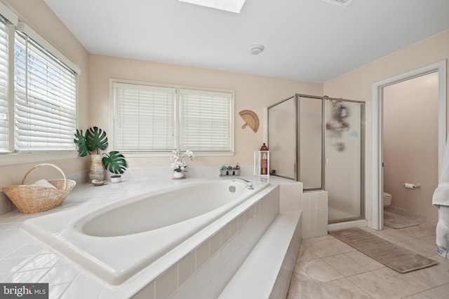 full bathroom with a stall shower, a skylight, a garden tub, and toilet