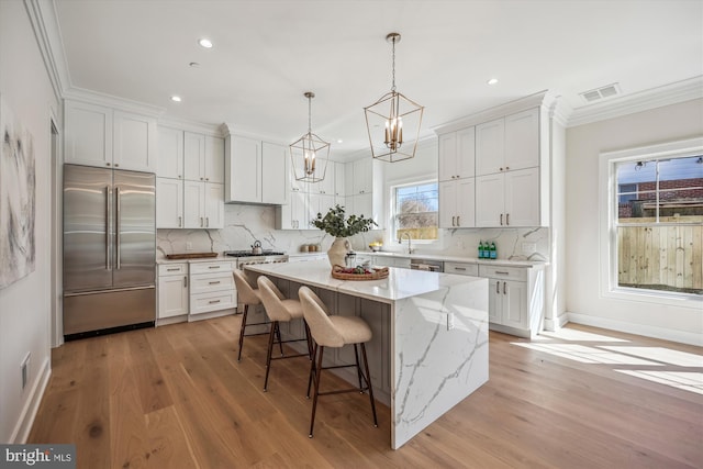 kitchen featuring light wood-type flooring, visible vents, built in fridge, a center island, and white cabinets