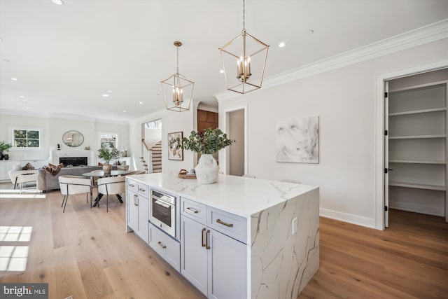 kitchen with a kitchen island, crown molding, light wood-style flooring, a fireplace, and hanging light fixtures