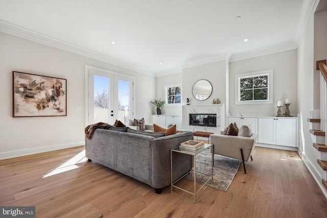 living area with a high end fireplace, french doors, crown molding, light wood finished floors, and baseboards