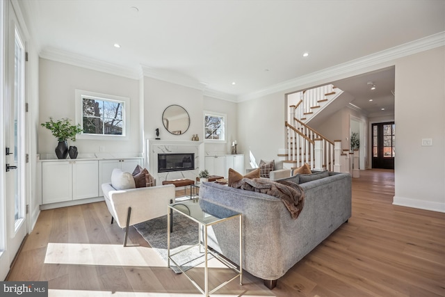 living area featuring recessed lighting, a high end fireplace, stairs, crown molding, and light wood-type flooring