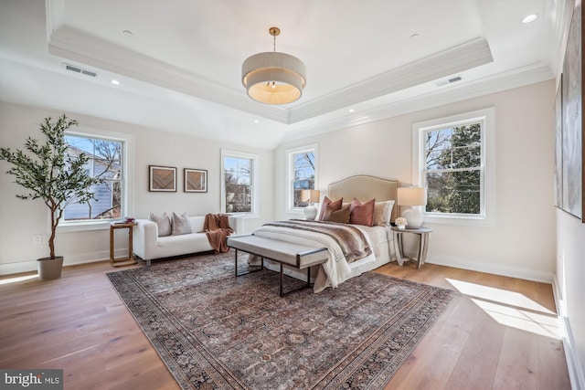 bedroom with a raised ceiling, multiple windows, wood finished floors, and visible vents