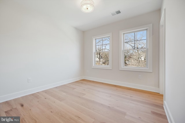 empty room featuring light wood finished floors, visible vents, and baseboards