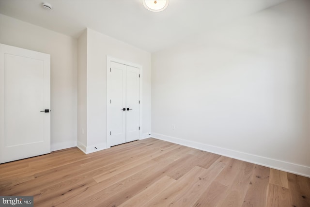 unfurnished bedroom with a closet, baseboards, and light wood-style floors