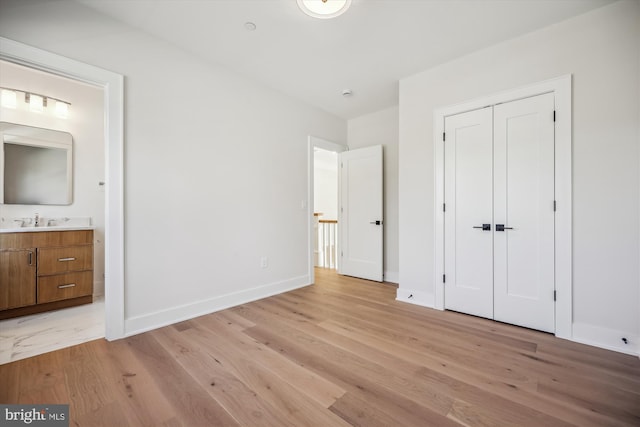 unfurnished bedroom featuring a sink, ensuite bath, a closet, light wood finished floors, and baseboards