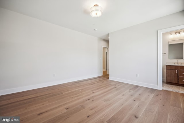 unfurnished bedroom featuring a sink, baseboards, ensuite bathroom, and light wood finished floors