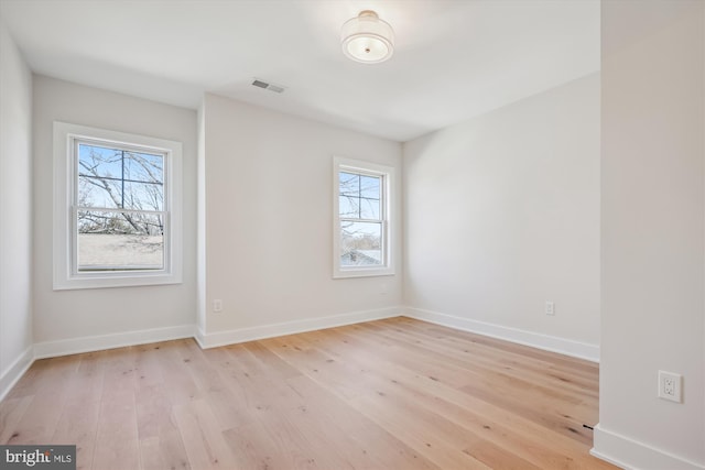 spare room with light wood finished floors, visible vents, and baseboards