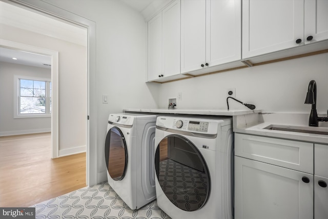 washroom featuring baseboards, washer and clothes dryer, light wood-style floors, cabinet space, and a sink