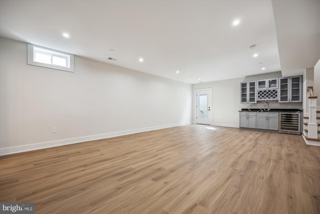 unfurnished living room with wet bar, recessed lighting, beverage cooler, and light wood-type flooring