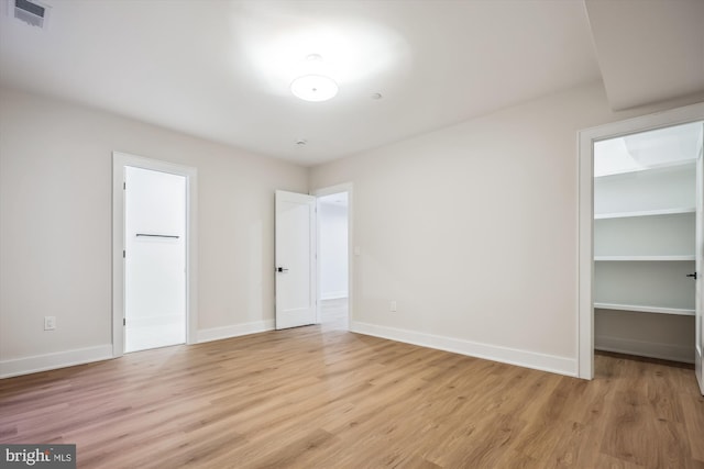 unfurnished bedroom featuring light wood-type flooring, visible vents, a walk in closet, a closet, and baseboards