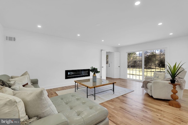 living room with recessed lighting, visible vents, wood finished floors, and a glass covered fireplace