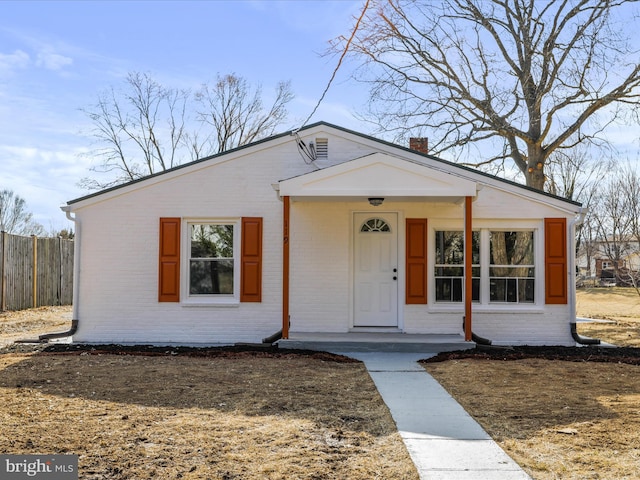 view of front facade with covered porch, brick siding, a chimney, and fence