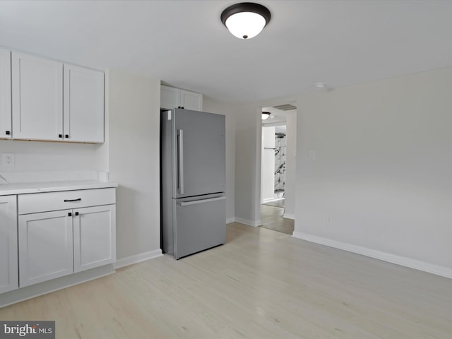 kitchen with light countertops, light wood-style floors, freestanding refrigerator, and white cabinetry