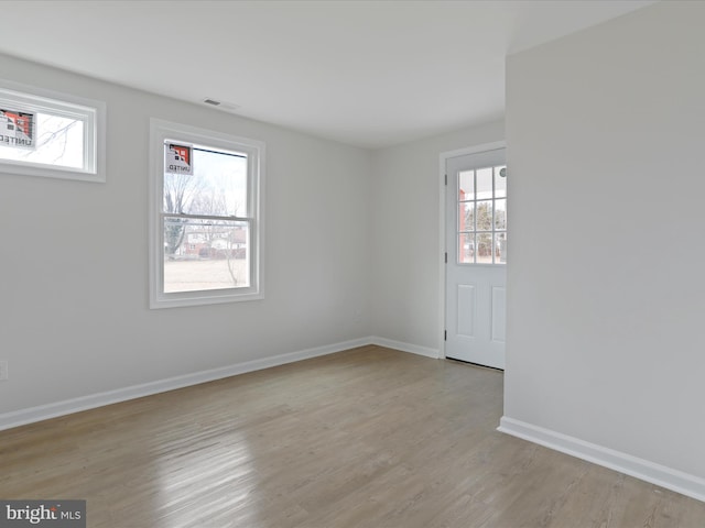 empty room featuring plenty of natural light, visible vents, baseboards, and light wood-style flooring