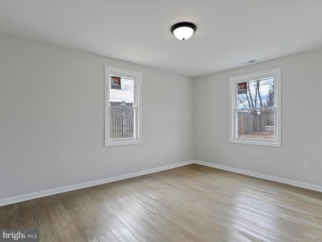 empty room with light wood-style floors, visible vents, and baseboards