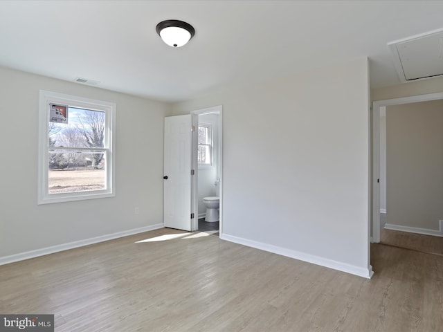 unfurnished bedroom featuring attic access, baseboards, visible vents, ensuite bath, and light wood-type flooring