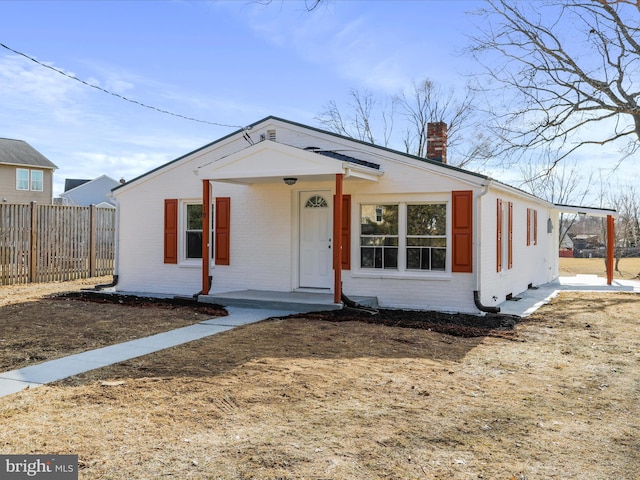 bungalow-style home with brick siding, fence, and a chimney