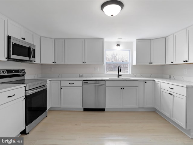 kitchen with light stone counters, stainless steel appliances, light wood-style floors, white cabinetry, and a sink