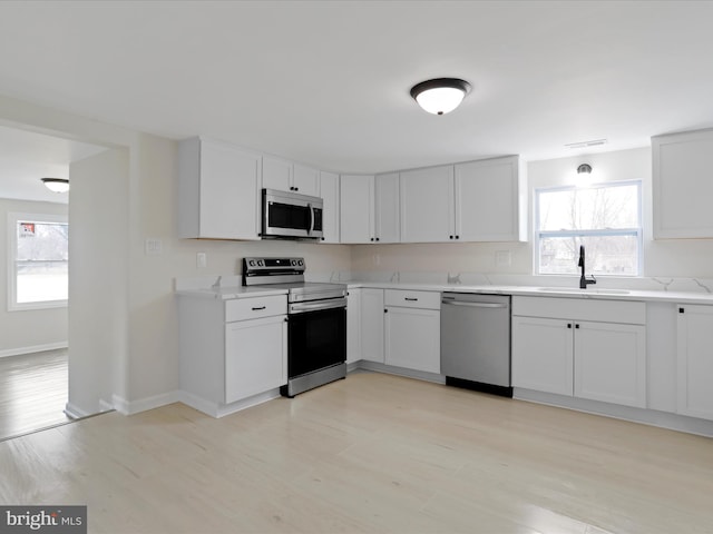 kitchen featuring stainless steel appliances, light countertops, white cabinetry, a sink, and plenty of natural light