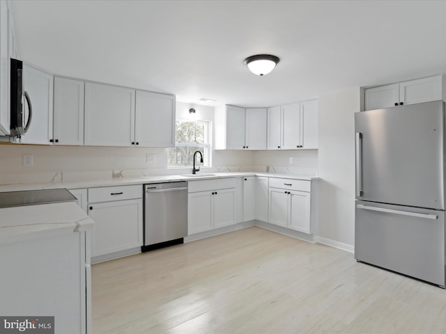 kitchen featuring light wood finished floors, light countertops, appliances with stainless steel finishes, white cabinets, and a sink