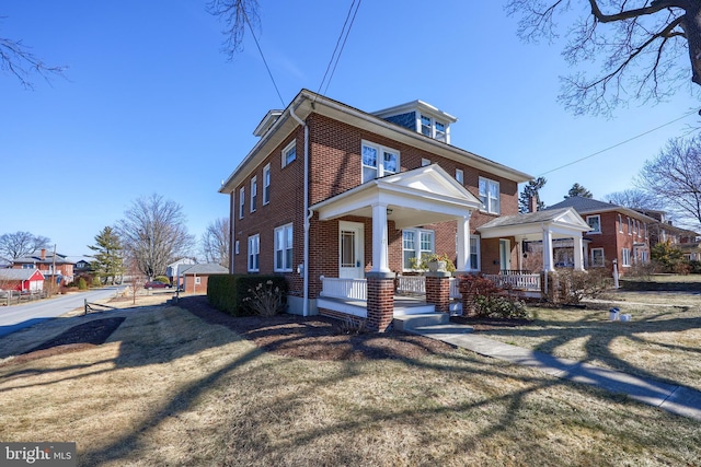 traditional style home with a front yard, covered porch, and brick siding